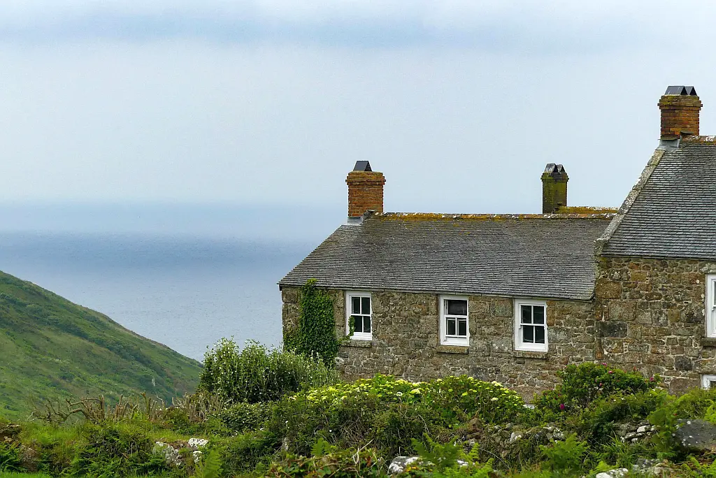 Sunset over a little white cottage with green lawn and the sea as backdrop