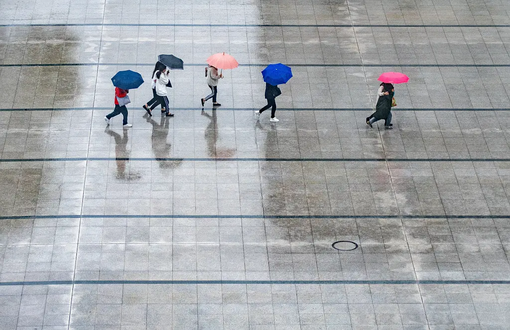 Reflection of young man with red umbrella in puddle on a rainy city street during rain.